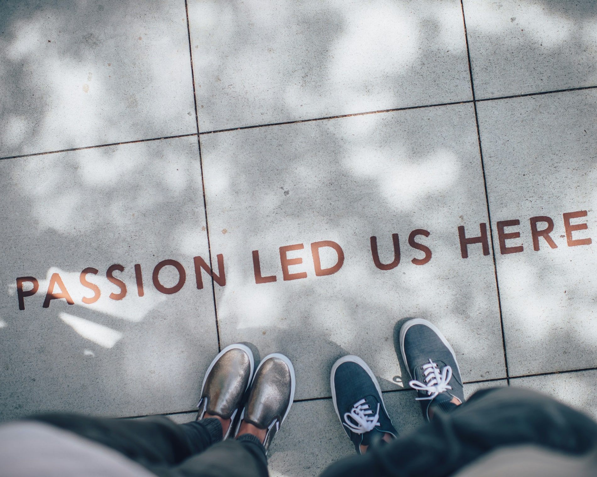 Two people looking down at a paved floor lettered with the words passion led us here
