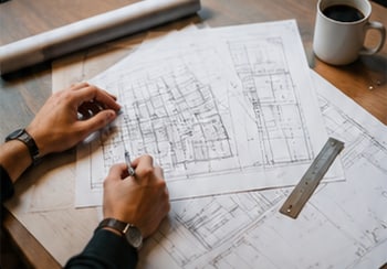 Hands drawing on a set of construction plans beside a ruler and a cup of coffee